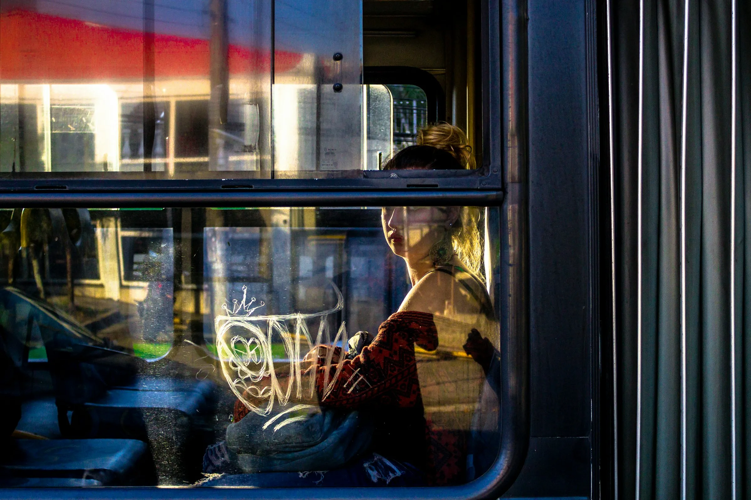 A woman looking through a bus window in warm evening light