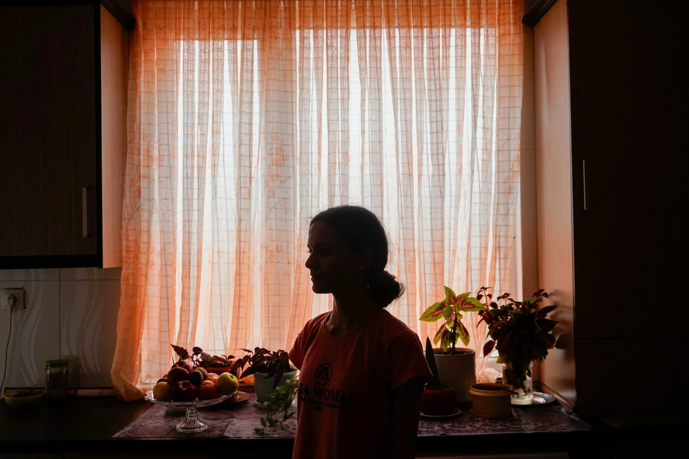 A woman silhouetted against warm light through a kitchen window